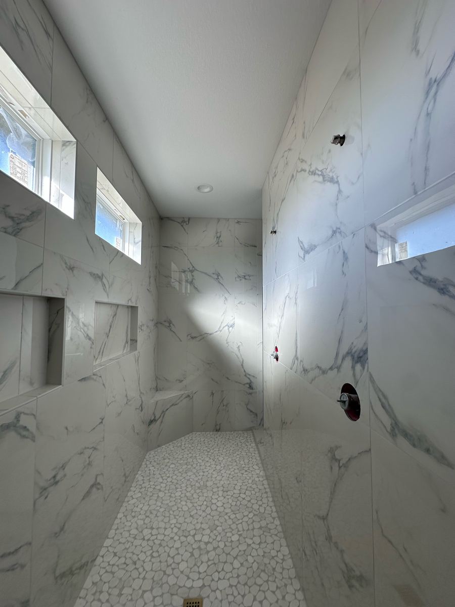 Project Pilot project: Long walk-in shower with large white marble-look wall tile, a white pebble floor, recessed niches, and high windows